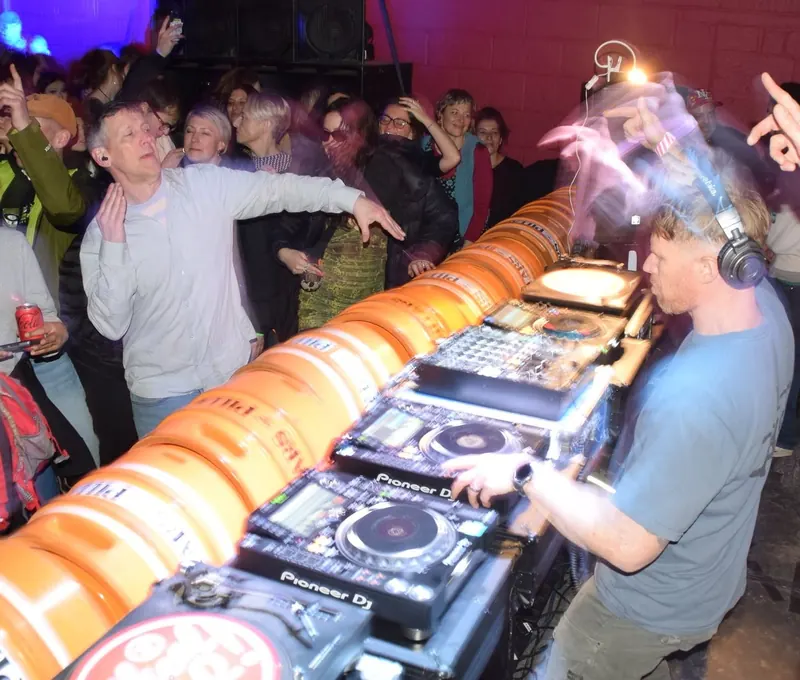 Scruff Baggins DJing behind a booth of orange kegs while the crowd dances