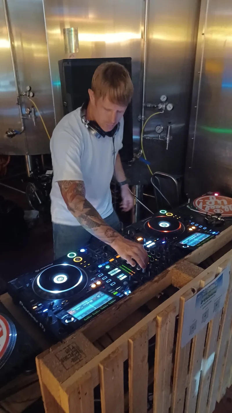 Scruff Baggins DJing on Pioneer decks in a brewery, surrounded by steel tanks