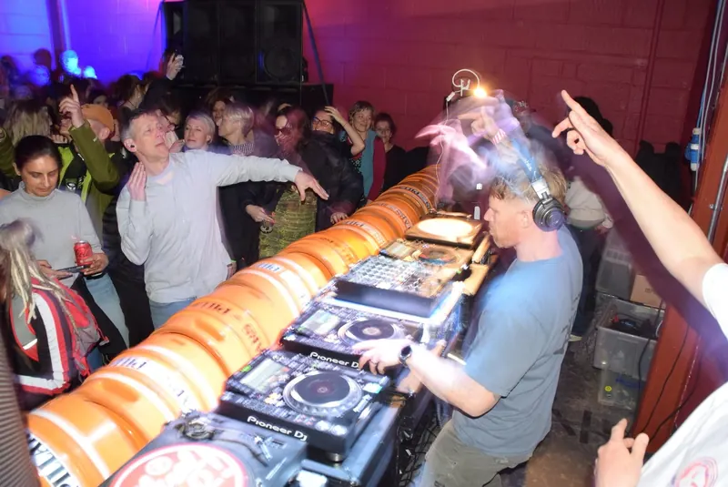 Wide shot of the party: Scruff Baggins at the decks, the crowd and the sound system behind
