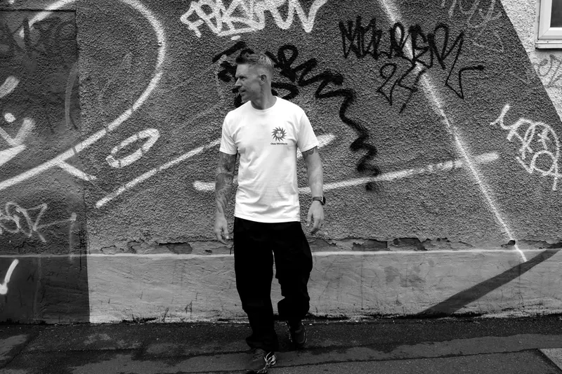 Black and white shot of Scruff Baggins walking past a graffiti wall